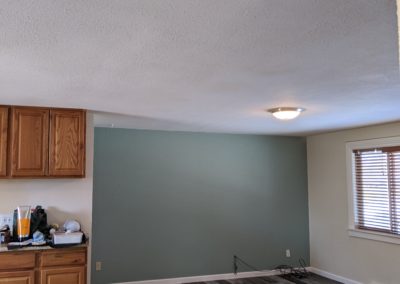 Looking into open kitchen and living room with patched ceiling drywall where wall was