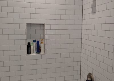 Bath products in shower nook and puff on new faucet in shower with subway tiles from the tub to ceiling