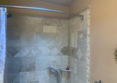 Shower with square tiles and a row of tiles on an angle to be diamond-shaped and hand-held shower head
