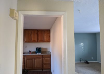 2. Kitchen cabinets and vinyl floor on left and living room with stained carpet on right with wall and doorway between them
