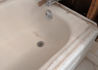Damaged bathtub with walls above it stripped to the studs and insulation and plumbing exposed
