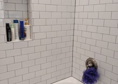 Toiletries in shower nook and subway tiles to ceiling above bathtub with smooth surface