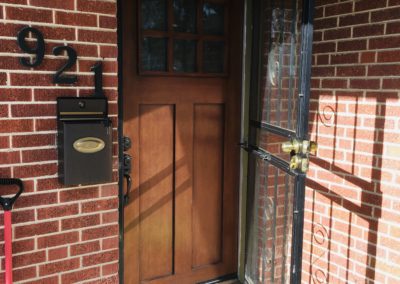 Open security door and new, dark wood 2-panel Shaker front door with 6-pane glass window at brick house