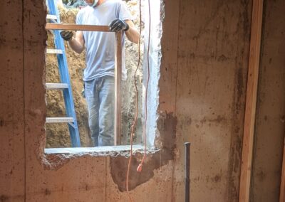IN PROGRESS: After the 9 ½” thick foundation wall was cut with a concrete saw, the center of the hole was knocked out with a sledgehammer. Then, a frame was added to structurally reinforce the hole before the new window is installed.