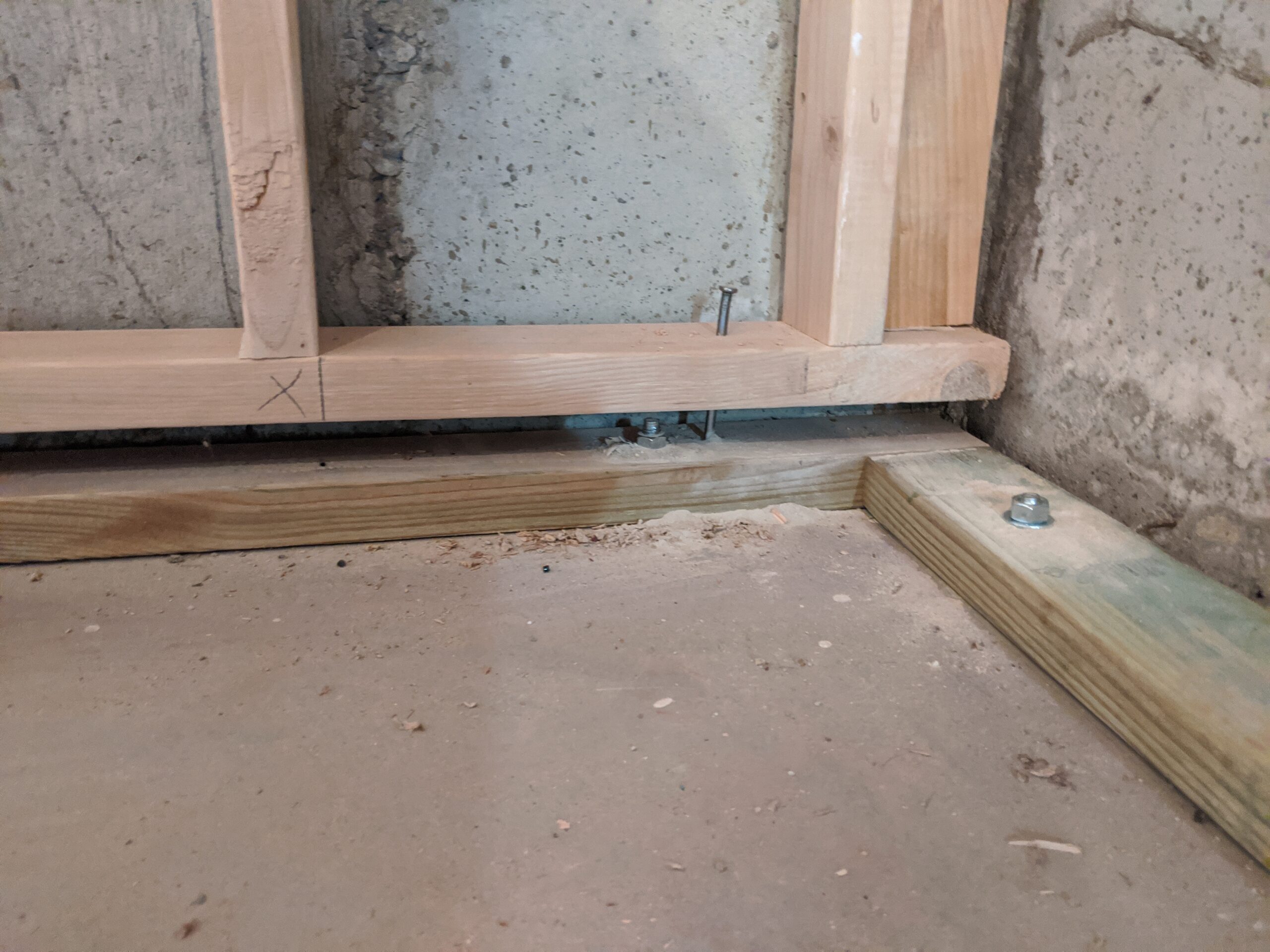 IN PROGRESS Here’s a close-up of a floating wall that’s framed correctly. Notice the gap below the wall and bolt through the bottom of the wall into the floor plate. The green tint of the floor plate indicates that it’s pressure-treated lumber that won’t rot when in direct contact with the concrete subfloor.