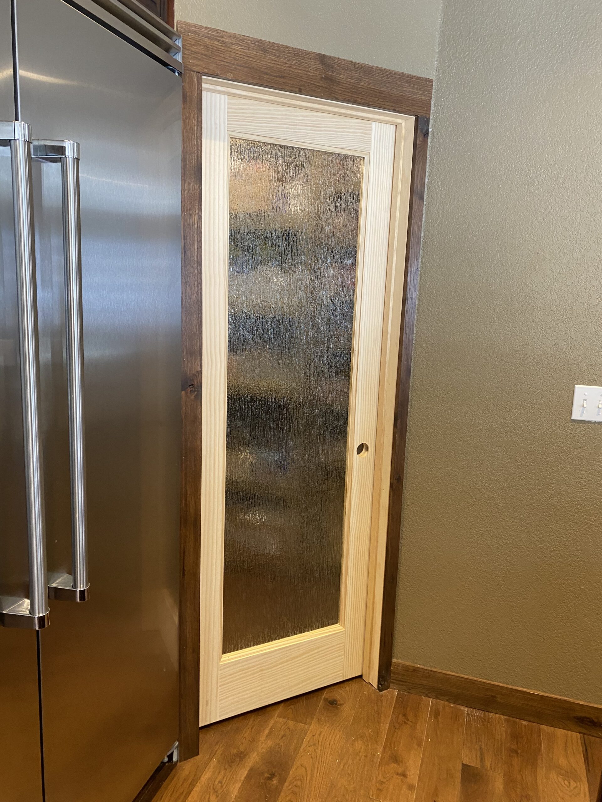 On right of stainless steel refridgerator is pine wood framed door with full pane of obscurity glass