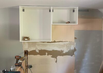kitchen DURING demo with new cabinet boxes hung on wall, exposed wooden subfloor, framing, and electrical wires