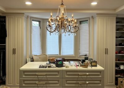 Custom walk-in closet with elegant chandelier lighting, built-in cabinetry, and large island drawers, softly illuminated by recessed lighting.