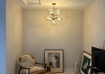 Modern reading nook with mid-century style armchair, plush rug, ottoman, and glass pendant light, styled with framed artwork and a cozy vibe.