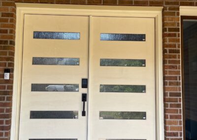 Modern double front doors with horizontal privacy glass inserts and matte black hardware set in a brick exterior entryway.”