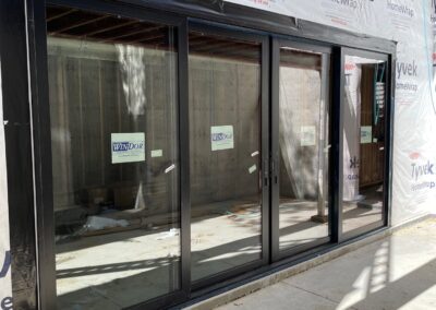 Exterior view of fully installed oversized sliding glass doors in a new residential build, sealed with Tyvek HomeWrap and surrounded by concrete patio.