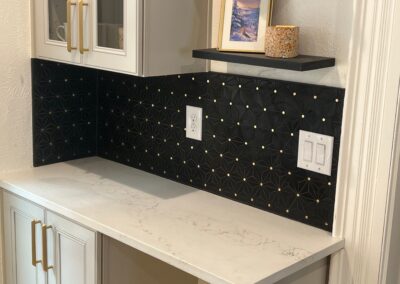 Corner view of a kitchen with black geometric backsplash tile, gold cabinet hardware, and sleek quartz countertops.