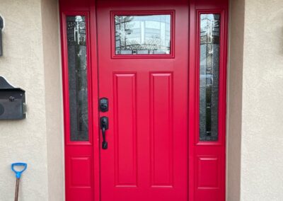 Exterior view of a bright red front door with glass sidelights, brick entry, and updated hardware