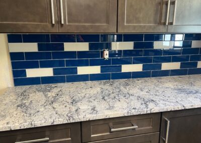 Glossy deep blue subway tile backsplash with white accent tiles above speckled granite countertops.