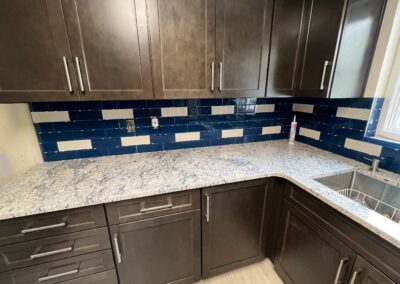 Modern kitchen with dark cabinetry, blue and white subway tile backsplash, and light granite countertops.