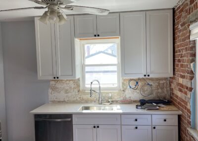 Bright kitchen with new white shaker cabinets, quartz countertops, exposed brick wall, and under-cabinet lighting.