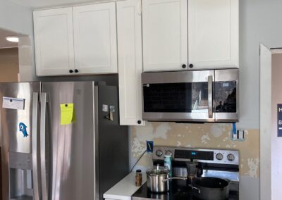 Custom-fit white shaker cabinetry installed around stainless steel refrigerator and microwave in updated kitchen.