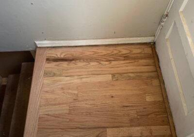 Restored hardwood floors at stairway landing with patched and refinished boards blending seamlessly.