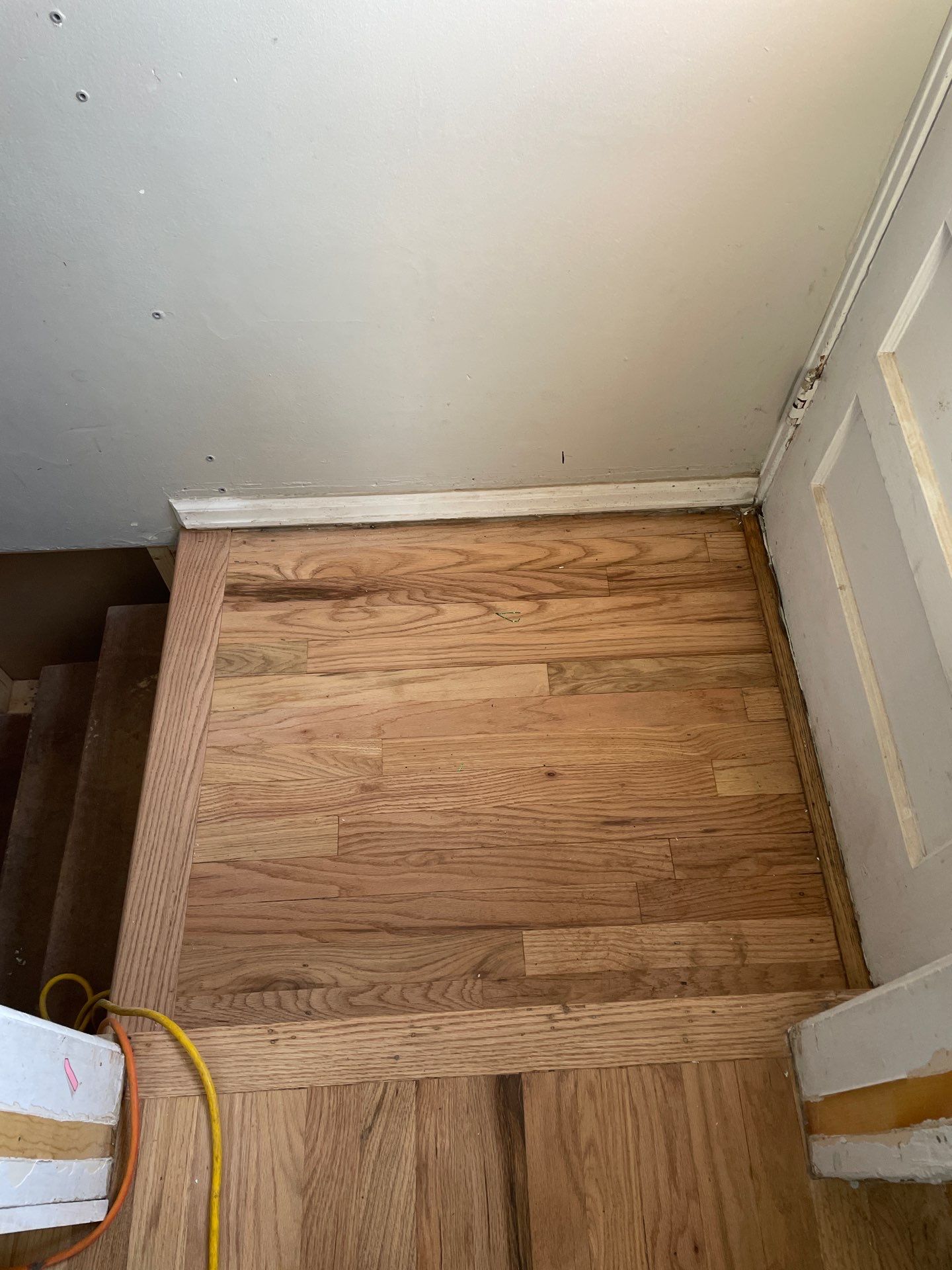 Restored hardwood floors at stairway landing with patched and refinished boards blending seamlessly.