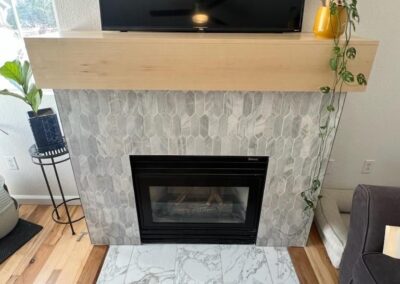 Completed fireplace with marble picket tile surround, custom wood mantel, and seamless marble hearth flush with hardwood floors.