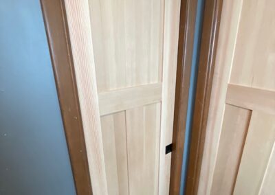 Close-up of newly installed wooden pocket doors in a blue-painted bathroom with natural trim and tile floors.