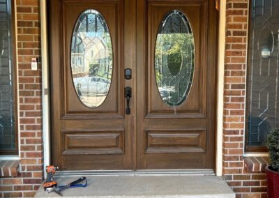 Traditional wood double entry doors with oval decorative glass and raised panels, framed by brick exterior walls.