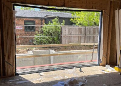 Interior view of framed wall with rough opening for large sliding glass door, showing subfloor, ceiling joists, and surrounding construction materials.
