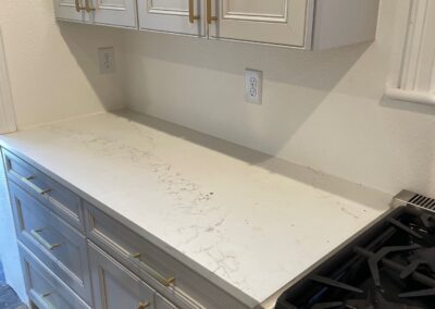 Close-up view of white cabinets and countertop before tile installation, showing blank wall space for future backsplash.