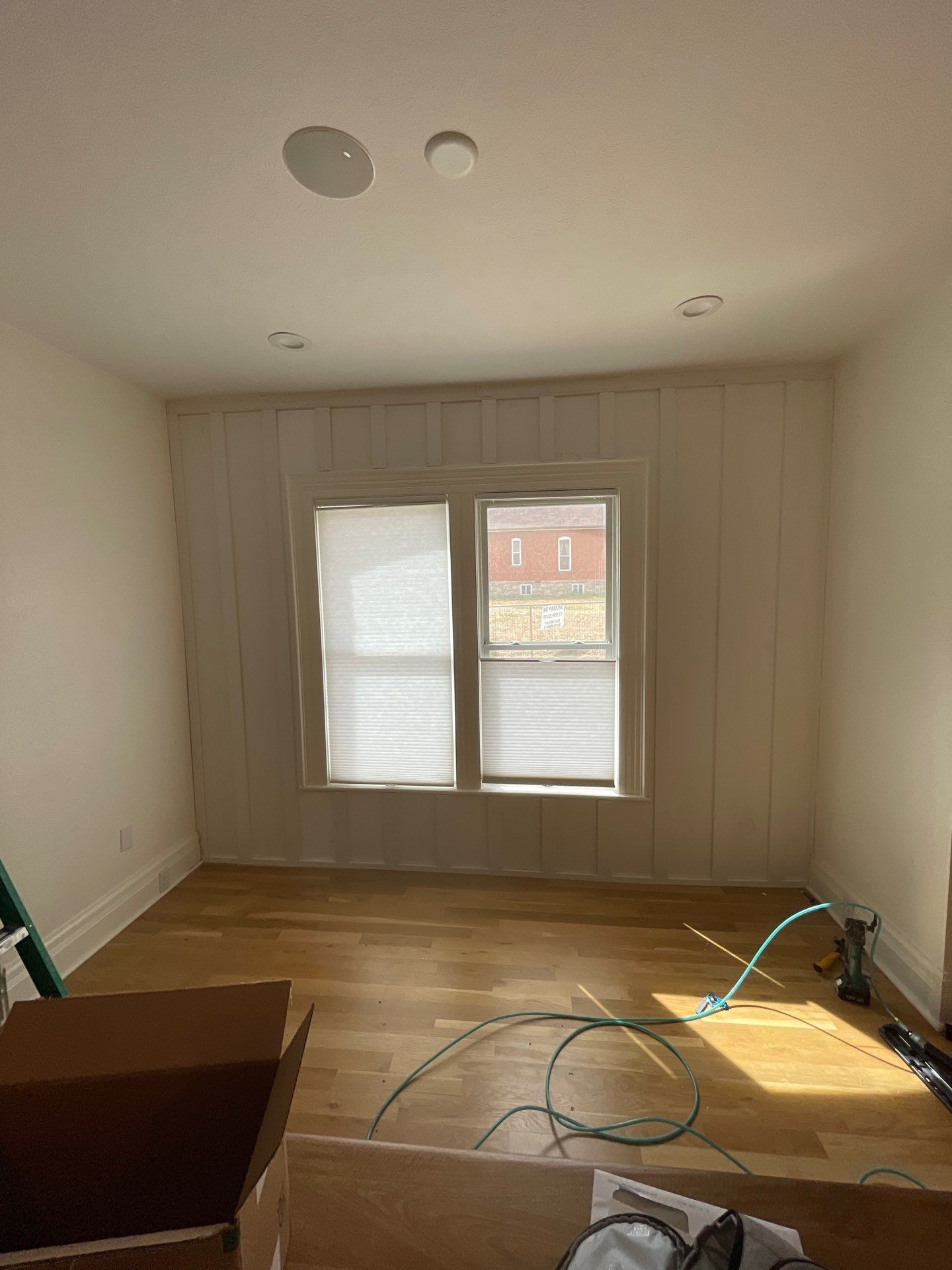 A work-in-progress shot of a room with wood floors, window trim, and visible electrical cords, showing natural light across unfinished walls.