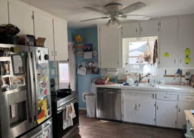 Outdated kitchen with white cabinets, tile countertops, blue walls, and ceiling fan in an old Denver home.