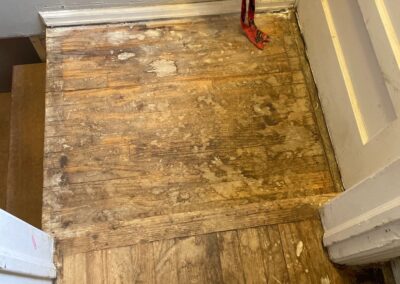 Worn and stained 80-year-old hardwood floors at the top of a basement stairwell in a historic home.