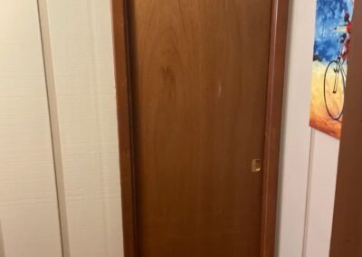 Older brown flush panel pocket door in a hallway with tan vertical panel walls and brown trim.
