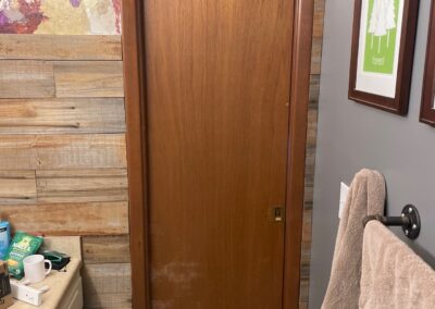 Outdated brown pocket door in a rustic-style bathroom with wood paneling and textured art on the wall.