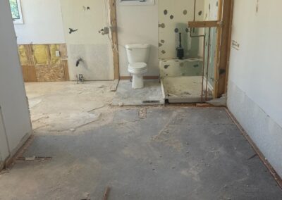 Demolition phase of a primary bathroom showing exposed plumbing, partial framing, and remnants of old fixtures.