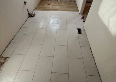 Close-up of large-format bathroom floor tiles during installation using red tile spacers and leveling clips.
