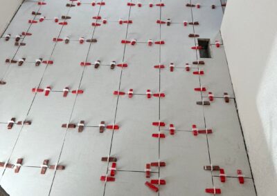 Newly installed large rectangular floor tiles in a bathroom with unfinished walls and exposed plumbing.