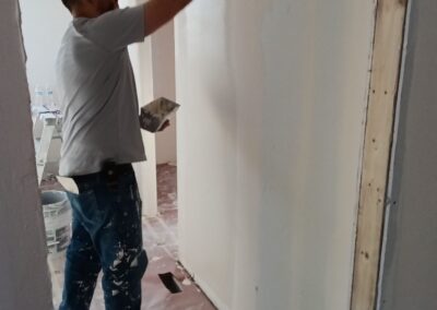 Contractor applying drywall compound to freshly hung drywall in a hallway under construction.