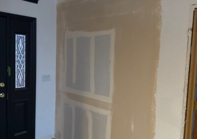 Drywall installation on a new interior wall near a front door entryway during renovation.