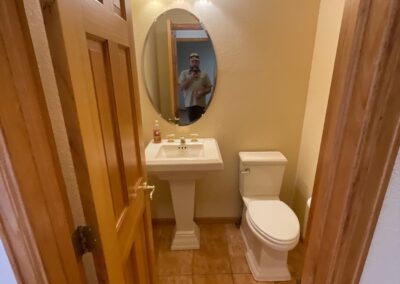 Small powder room with pedestal sink and toilet before renovation, featuring dated tile and lighting.