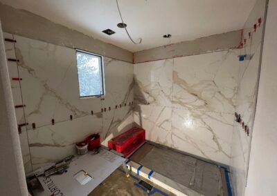 Shower tile installation underway with large marble-style slabs and corner bench completed.