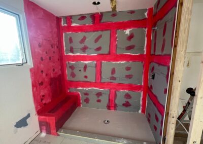 Shower walls prepped with red waterproof membrane over cement board, including a built-in bench.