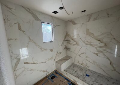 White marble-look tile being installed in a large walk-in shower during remodeling.