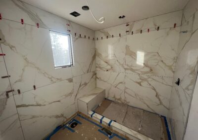 Shower walls partially tiled with large-format marble-pattern tiles and tile leveling clips.