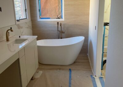 Modern freestanding soaker tub installed against textured feature wall in a renovated bathroom.