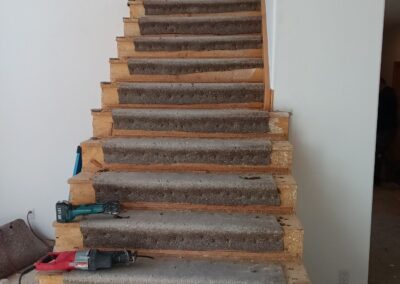 Staircase mid-renovation with carpet partially removed and power tools on steps.