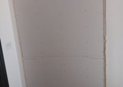 Freshly installed drywall panel on entry wall with construction debris on the floor.