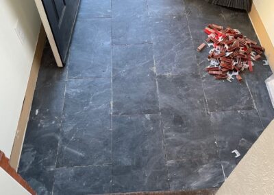 Entryway showing black slate tiles partially installed with tile spacers and a visible transition to outdoor pavers.