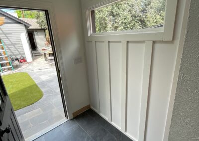 Board and batten paneling in progress on the angled entry wall with a slim rectangular window and black slate tile flooring below.