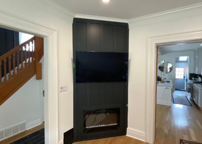 Electric fireplace installed within new board and batten wall, TV mounted above, unpainted paneling visible.
