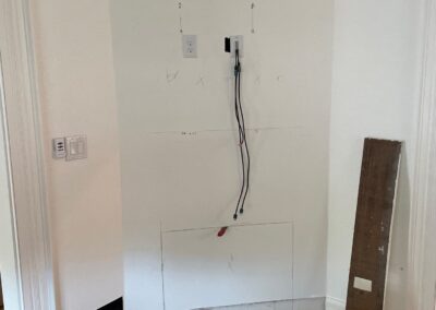 Living room corner with marked drywall and exposed wiring for the new electric fireplace and mounted TV.